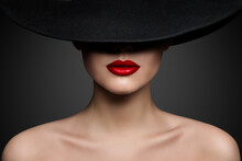 Red Lips Make Up Closeup. Mysterious Fashion Woman Face Hidden By Black Brimmed Hat. Elegant Retro Lady Fine Art Portrait Over Gray Background