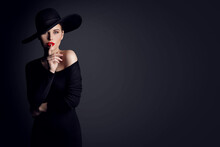 Fashion Woman Model In Hat Showing Shh Sign Of Silent Gesture Putting Finger In Red Lips. Elegant Lady In Black Dress Over Gray Studio Background