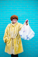 Smiling Senior Woman Holding Mesh Bag With Plastic Bottles In Front Of Turquoise Brick Wall