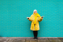 Senior Woman Gesturing On Footpath In Front Of Turquoise Brick Wall