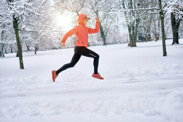 Running woman, girl runner on snow in park in winter sunny day. Female in pink sportswear jacket fitness training outdoors. Run, Sport concept, leisure and freedom.
