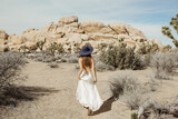 Fototapeta Boho - Woman in boho style dress and hat rushing through the Joshua Tree desert landscape