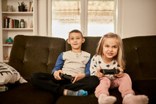 Brother And Sister Playing Video Game Sitting On Sofa At Home