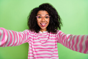 Sticker - Self-portrait of attractive cheerful crazy foolish girl showing tongue out teasing isolated over bright green color background