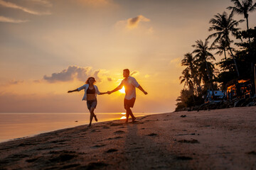Wall Mural - Young happy couple dancing on tropical beach at sunset, honeymoon travel concept
