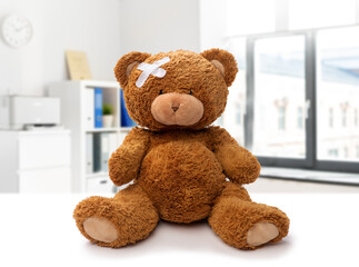 Wall Mural - medicine, healthcare and childhood concept - teddy bear toy with medical patch on head over hospital background