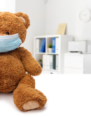 Wall Mural - medicine, healthcare and pandemic concept - teddy bear toy in protective medical mask over hospital background