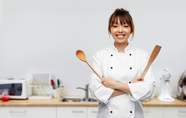 Poster - cooking, culinary and people concept - happy smiling female chef in toque with wooden spoon over restaurant kitchen background