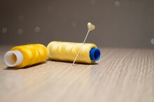 Two Yellow Spools Of Thread And Pin On Table On Blurry Backgroun