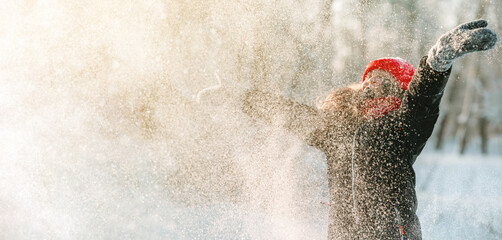 A little girl in a red hat and scarf throws snow up. Snowflakes in the winter forest