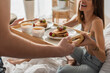 cropped view of man holding tray with pancakes and coffee near sexy and happy woman in bedroom.