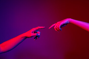 two human hands trying to touch each other isolated on purple background in neon light. concept of h