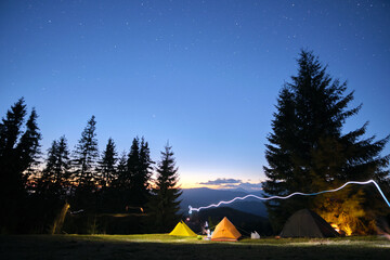 brightly illuminated camping tents glowing on campsite in dark mountains under night stars covered s