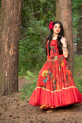 Gypsy woman. Red long dress. Portrait of a girl in an ethnic costume in the forest. The gypsy brunette is beautiful.