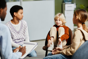 portrait of cute blond boy speaking in therapy session with diverse group of children