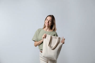 Wall Mural - Happy young woman with blank eco friendly bag on light background