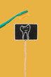 © Nastassia Kudzina - Smiling tooth drawing on a small black chalk board and a toothbrush on a minimal bright yellow background with copy space. Dentist and orthodontist concept. Hygiene for kids mock up.