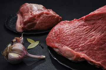 Wall Mural - Raw steak beef meat and pig fillet ready to cook. Fresh cut of beef on a black plates with spices. Selective focus