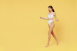 Full body young smiling happy satisfied brunette woman 20s wear white underwear with perfect fit figure hold measure tape on waist walk going isolated on plain yellow color background studio portrait.