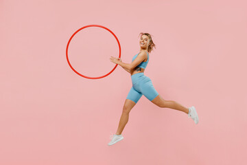 Full body young strong sporty athletic fitness trainer instructor woman wear blue tracksuit spend time in home gym hold hula hoop isolated on pastel plain light pink background. Workout sport concept.