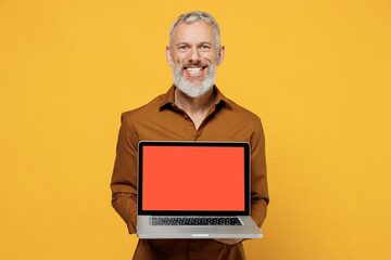 Wall Mural - Happy excited elderly gray-haired bearded man 40s years old wears brown shirt hold use work on laptop pc computer with blank screen workspace area isolated on plain yellow background studio portrait.