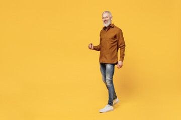 Full size body length excited charismatic fun elderly gray-haired bearded man 40s years old wears brown shirt looking camera smiling go move stroll isolated on plain yellow background studio portrait.