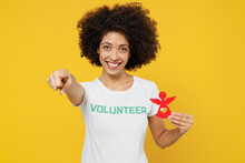 Young Woman Of African American Ethnicity Wears White Volunteer T-shirt Hold Little Paper Angel Point Finger Camera On You Isolated On Plain Yellow Background. Voluntary Free Work Help Grace Concept.