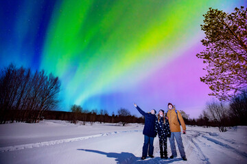 company of friends tourist looks aurora northern lights night at forest, soft focus