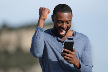 Man with black skin celebrating checking phone