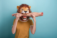 Young Woman In Lion Mask With Bitten Off Hand In Her Mouth, Isolated On Blue Background.