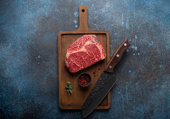 Canvas Print - Raw meat beef marbled prime cut steak Ribeye on wooden cutting board and rustic concrete kitchen table background from above with big knife and spices, beefsteak concept