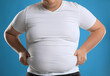 Overweight man in tight t-shirt on light blue background, closeup