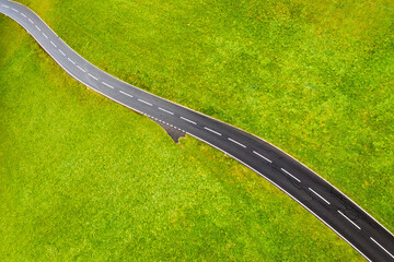 Poster - A straight road in a green meadow. Asphalt and grass. An aerial landscape from a drone as a backdrop. Swiss landscape