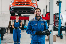 Male And Female Mechanics Working Together In Large Modern Car Repair Service.