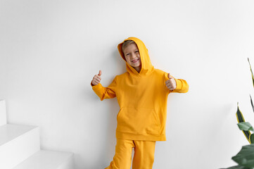 Wall Mural - a teenager in a yellow tracksuit on a monochrome background in a hood shows super