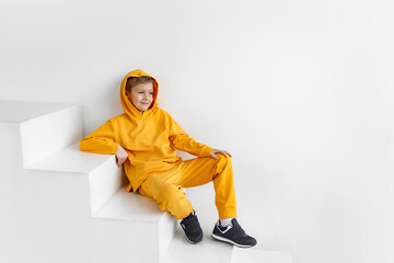 Wall Mural - a teenager in a yellow tracksuit on a monochrome background in a hood is sitting on the steps