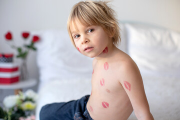 Wall Mural - Beautiful blond toddler child, boy with lipstick kisses on his body, holding red rose for Valentine