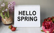 © Tatyana - A notepad with the inscription hello spring stands on the table next to a vase with lilac branches. Around decorative flowers, strawberries. Conceptual photo.