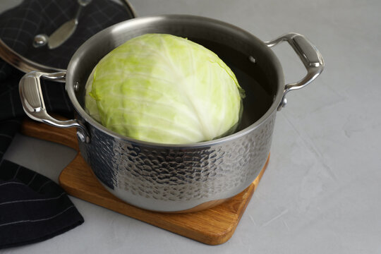 Sauce pan with hot water and cabbage for preparing stuffed rolls on light grey table