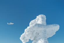 Light Airplane Moving In Blue Sky Behind Giant Cross In Snow