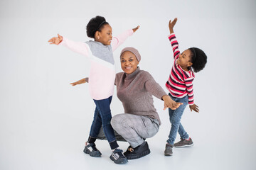 Poster - Two little cheerful sisters and their pleasant lovely mother playing together in white studio. African american family enjoying common leisure activity.