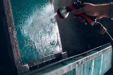 Wall Mural - Male worker cleaning screen frame with water in a printing workshop