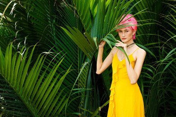 Wall Mural - Fashion Poses of Pink dying hair woman wear yellow dress and look strong over tropical green leaves