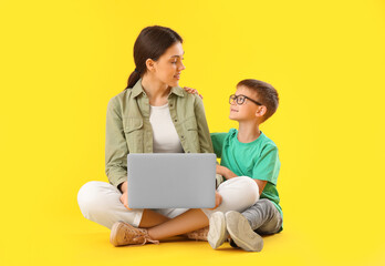 Wall Mural - Little boy with his older sister using laptop on yellow background