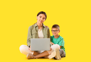 Wall Mural - Little boy with his older sister using laptop on yellow background