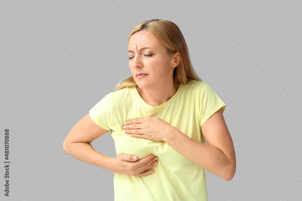 Mature woman feeling discomfort in her breast on grey background. Cancer awareness concept