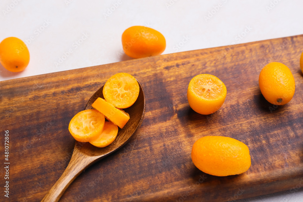 Spoon with tasty kumquat fruits on light background