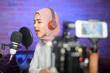 Young smiling muslim female singer wearing headphones with a microphone while recording song in a music studio with colorful lights.