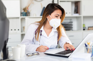 Wall Mural - Woman doctor in medical mask is working at laptop in clinic