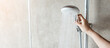 © Jo Panuwat D - Hand holding shower head during taking shower with wall background in modern bathroom